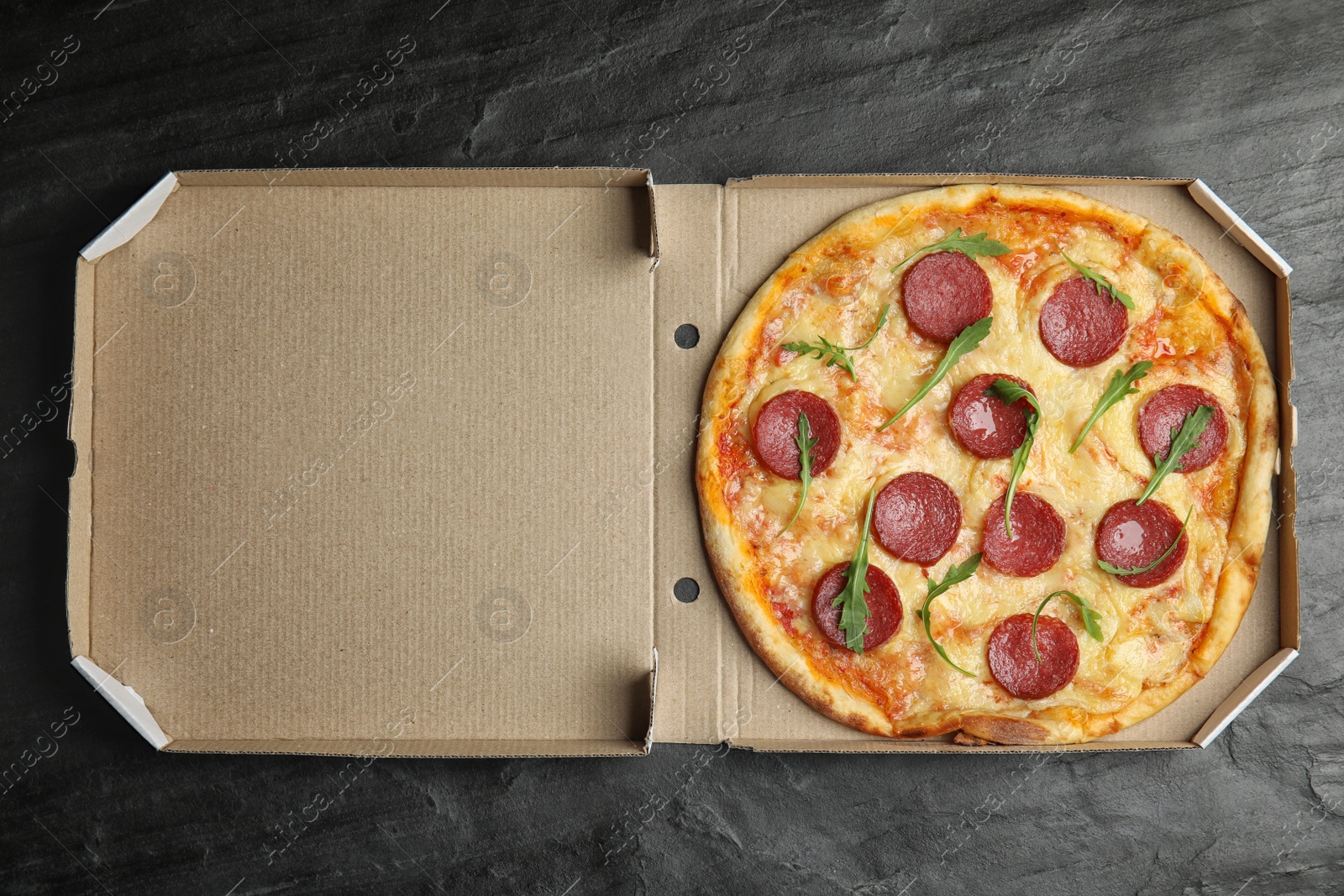 Photo of Tasty pepperoni pizza in cardboard box on black table, top view