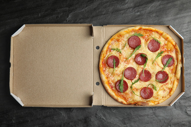 Tasty pepperoni pizza in cardboard box on black table, top view