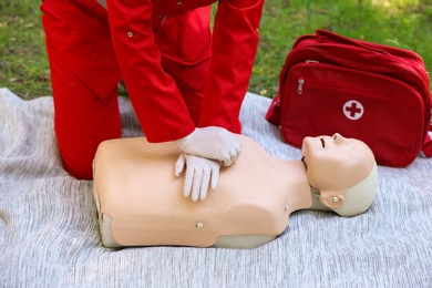 Photo of Woman in uniform practicing CPR on mannequin at first aid class outdoors
