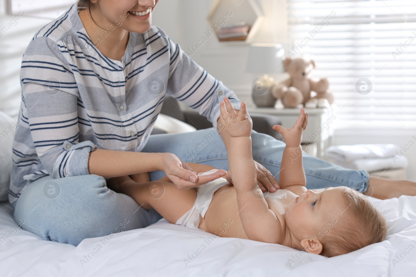 Photo of Mother applying dusting powder on her cute baby at home, closeup