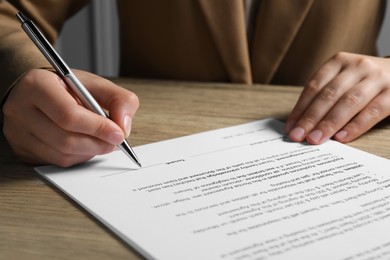 Photo of Woman signing document with pen at wooden table, closeup