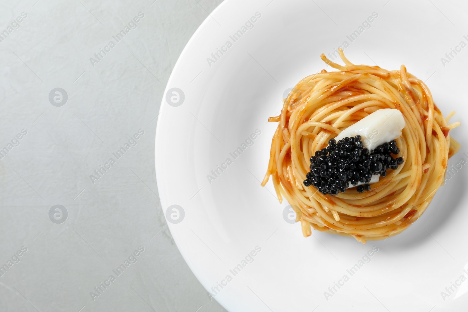 Photo of Tasty spaghetti with tomato sauce and black caviar on light grey table, top view. Exquisite presentation of pasta dish