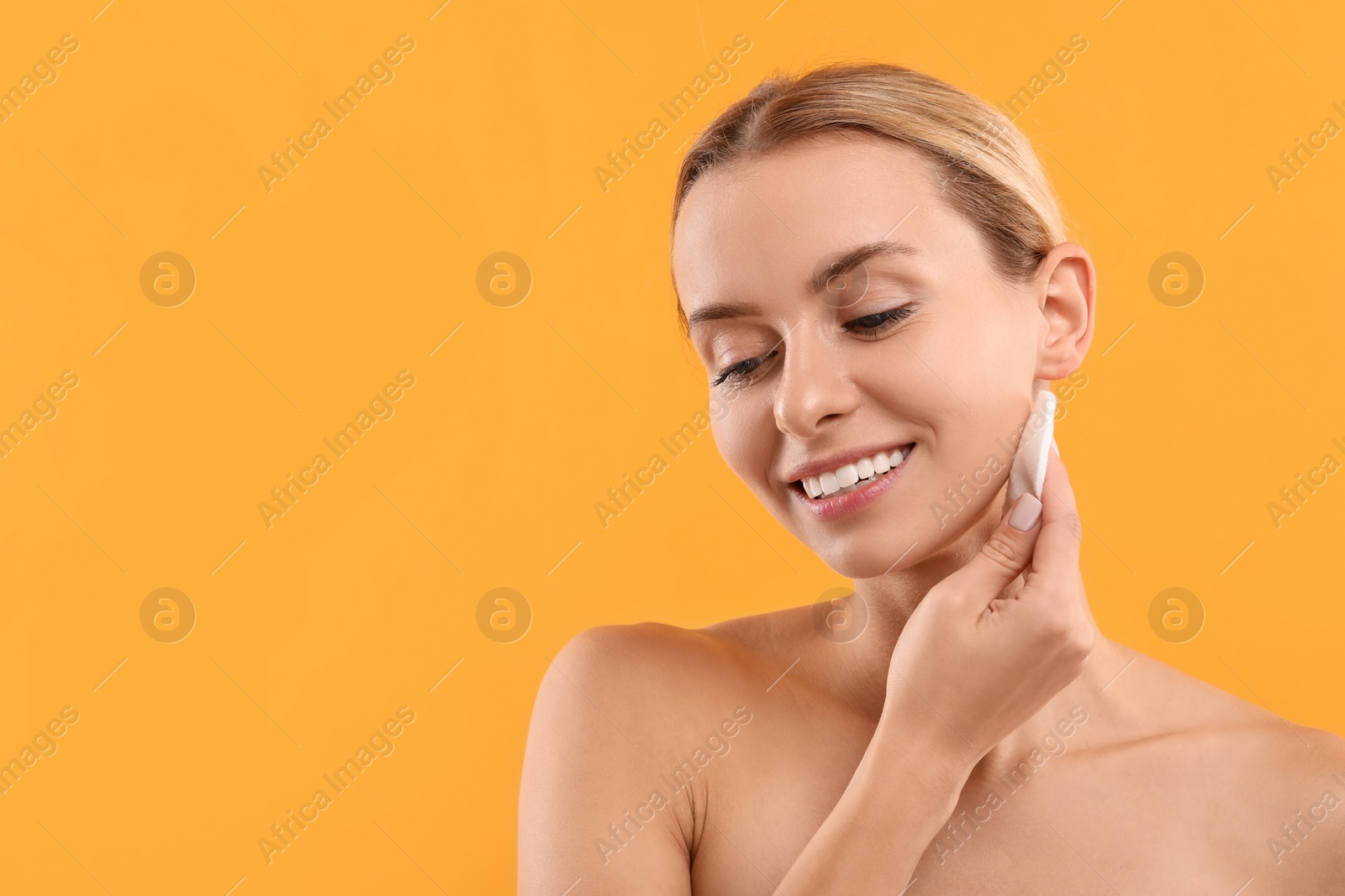 Photo of Smiling woman removing makeup with cotton pad on yellow background. Space for text