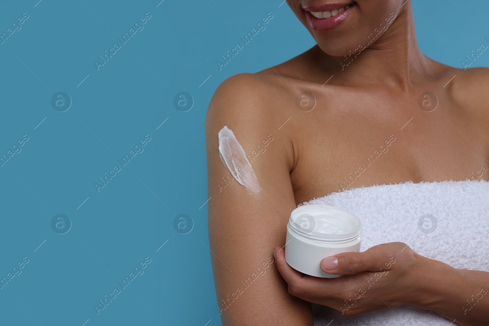 Photo of Young woman applying body cream onto arm on light blue background, closeup. Space for text