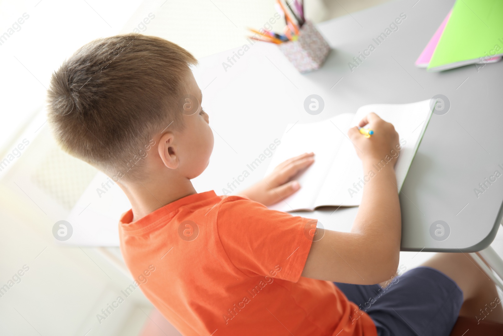 Photo of Cute little child doing assignment at desk in classroom. Elementary school