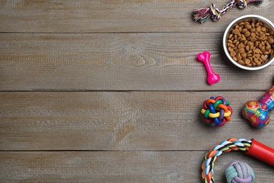 Flat lay composition with different pet toys and feeding bowl on wooden background, space for text