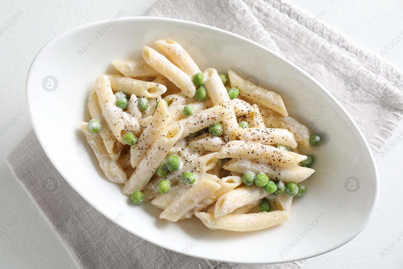 Photo of Delicious pasta with green peas and creamy sauce in bowl on white table, top view