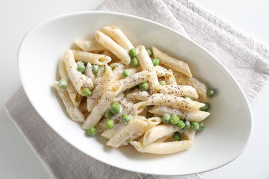 Delicious pasta with green peas and creamy sauce in bowl on white table, top view