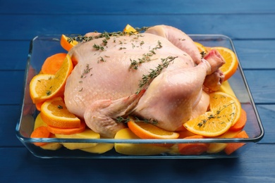 Photo of Raw chicken with orange slices, potatoes and thyme on blue wooden table