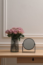 Mirror and vase with pink roses on wooden dressing table in makeup room