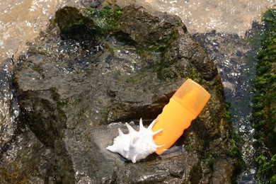 Photo of Bottle with sun protection spray and seashell on rock near sea tide, top view. Space for text