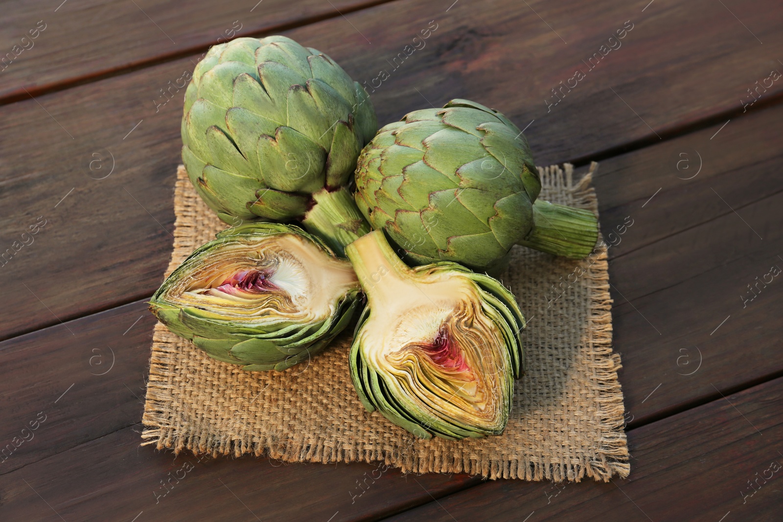 Photo of Whole and cut fresh raw artichokes on wooden table
