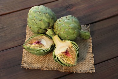 Whole and cut fresh raw artichokes on wooden table