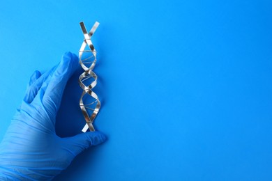 Photo of Scientist with DNA molecular chain model made of metal on blue background, closeup. Space for text