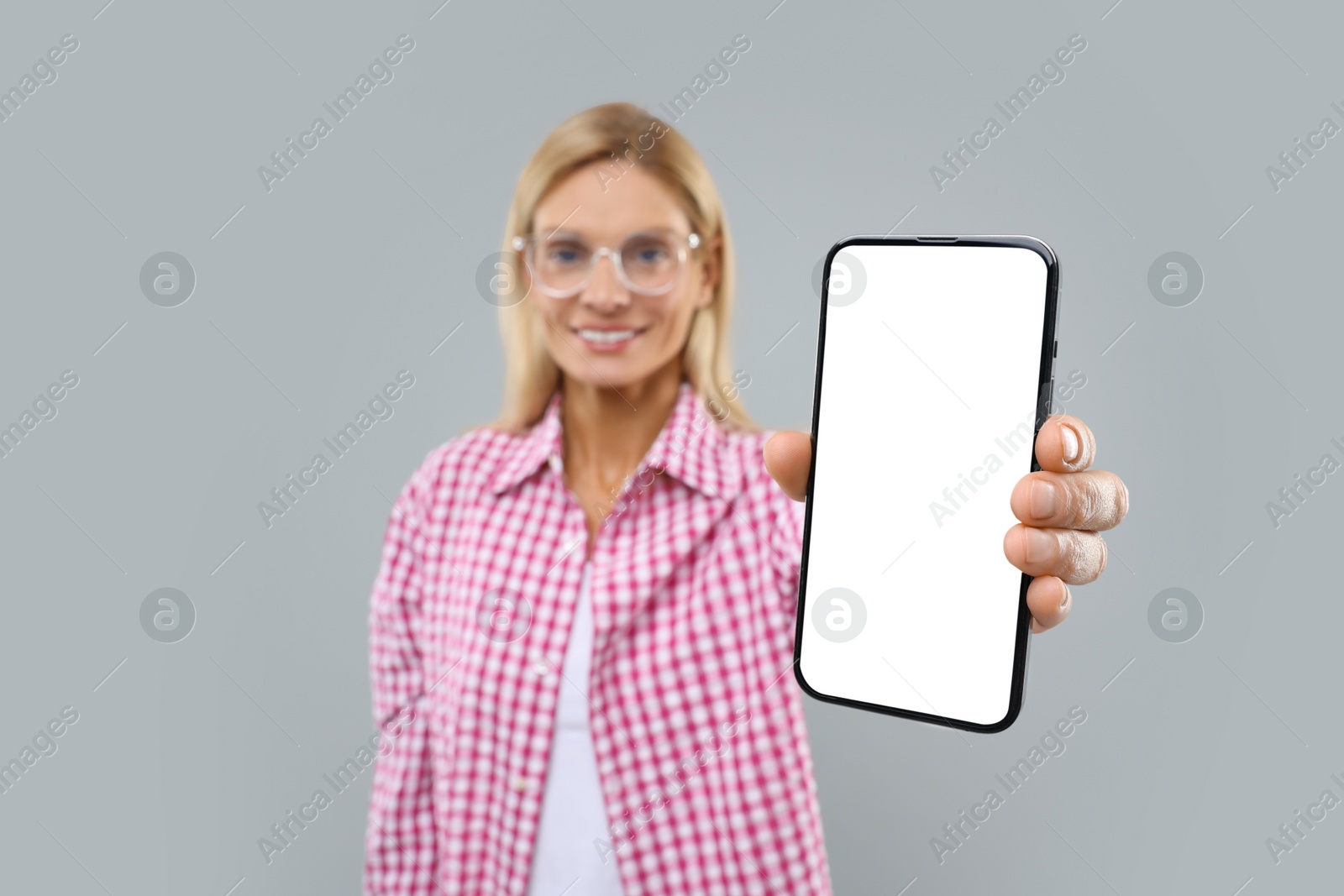 Photo of Happy woman holding smartphone with blank screen on grey background, selective focus