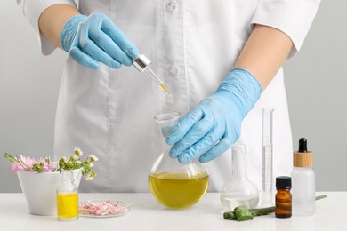 Scientist developing cosmetic oil at white table, closeup