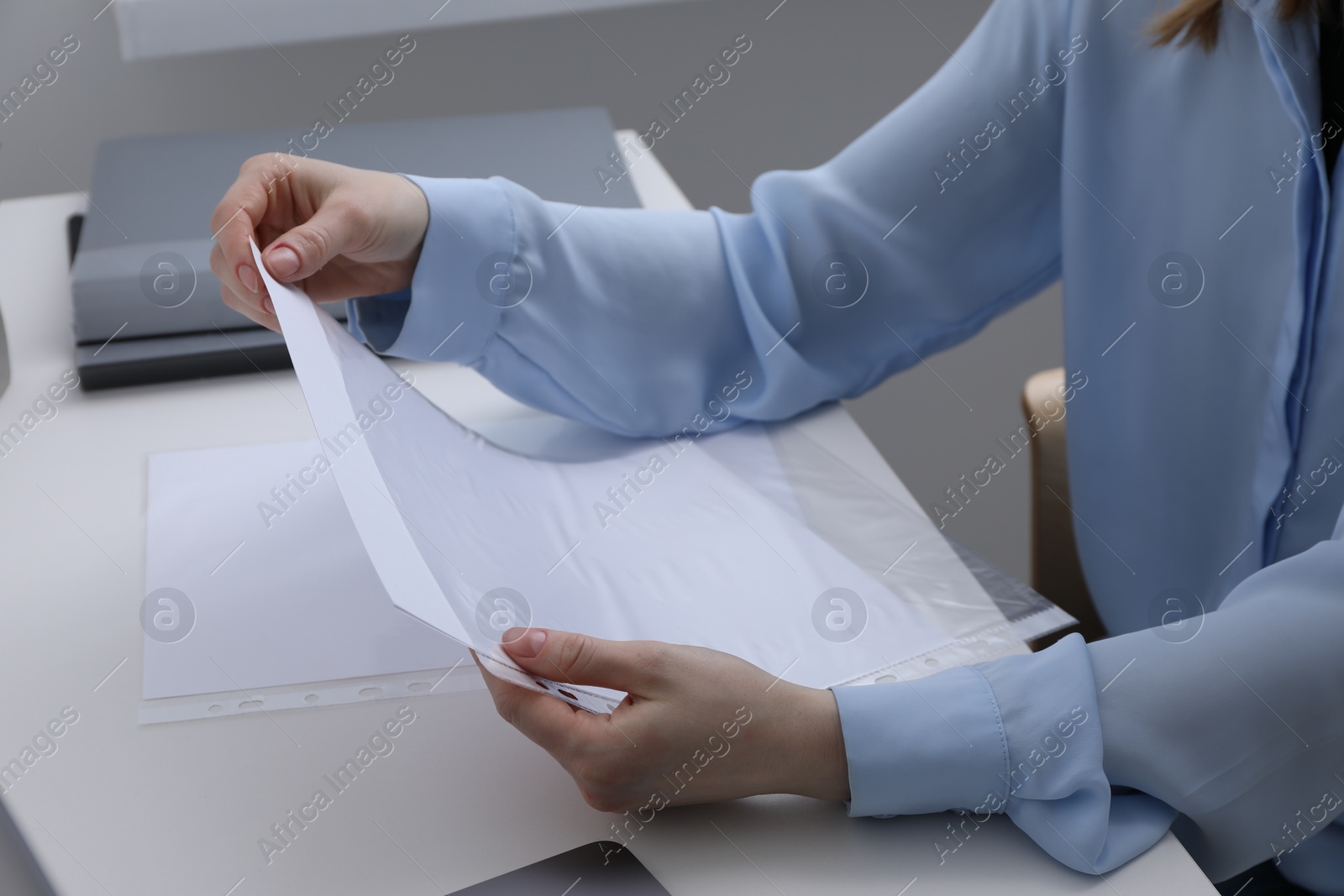 Photo of Woman putting paper sheet into punched pocket at white table, closeup