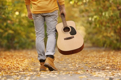 Photo of Young man with guitar walking in autumn park, closeup