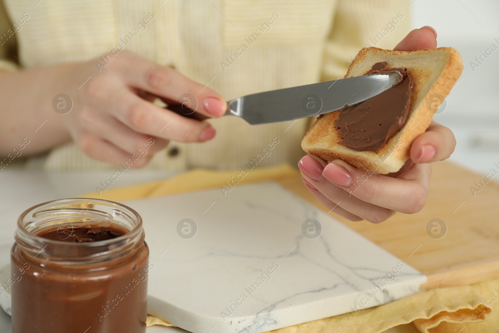 Photo of Woman spreading tasty nut butter onto toast at table, closeup