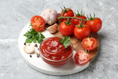 Delicious ketchup in bowl, parsley, garlic and tomatoes on grey textured table, closeup