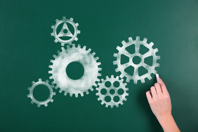 Woman drawing gear mechanism on chalkboard, closeup 