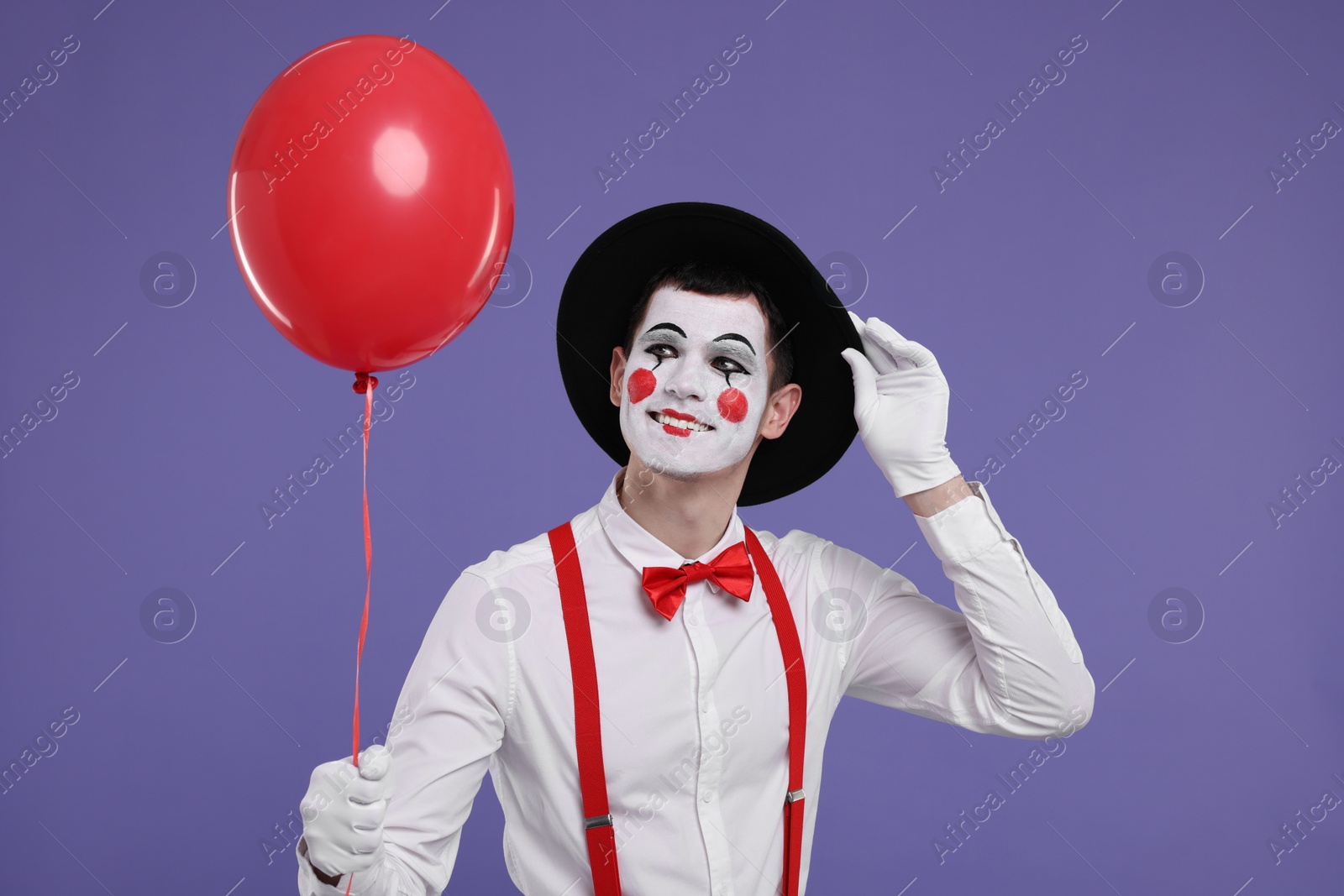 Photo of Funny mime artist with red balloon on purple background