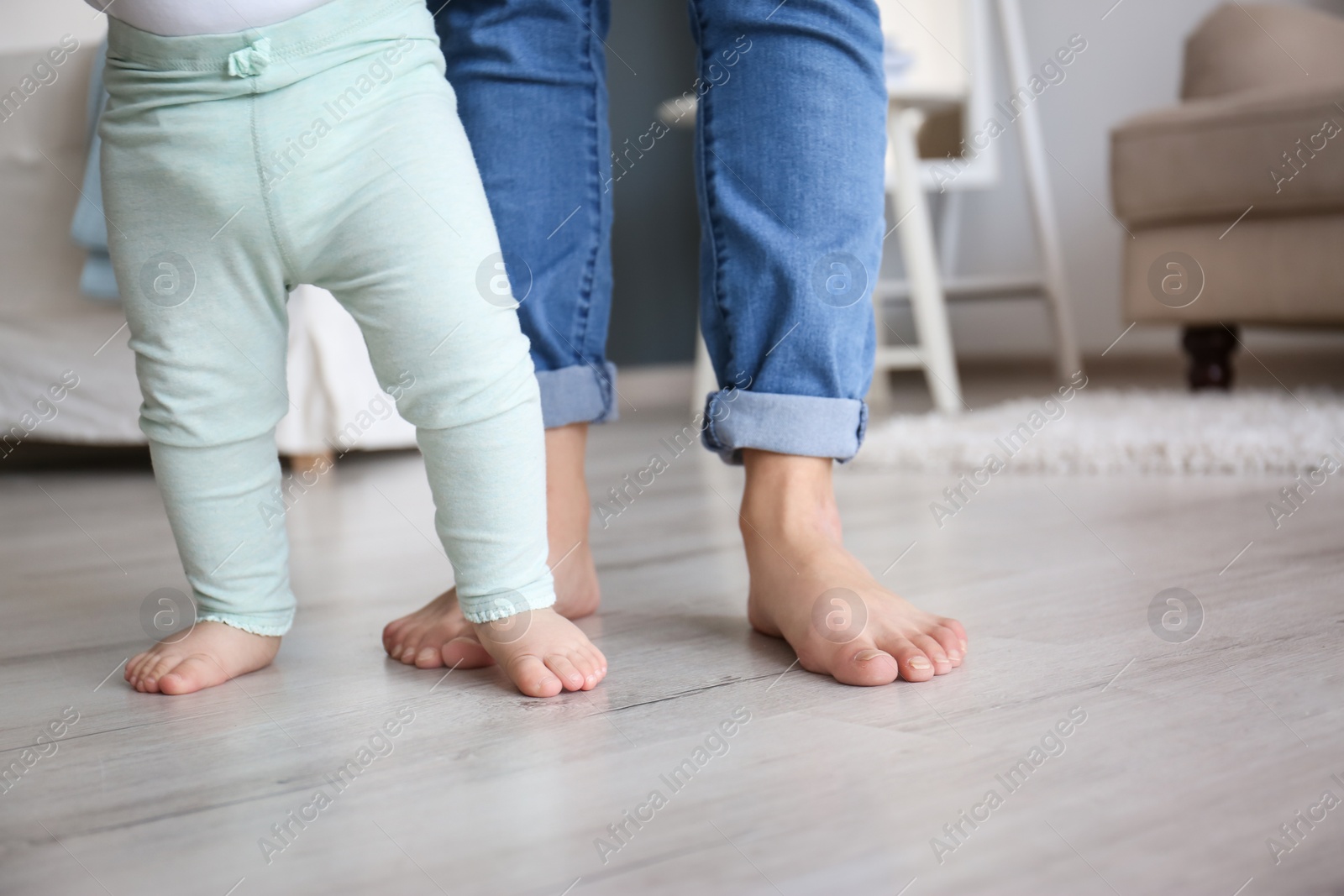 Photo of Baby doing first steps with mother's help, closeup of legs