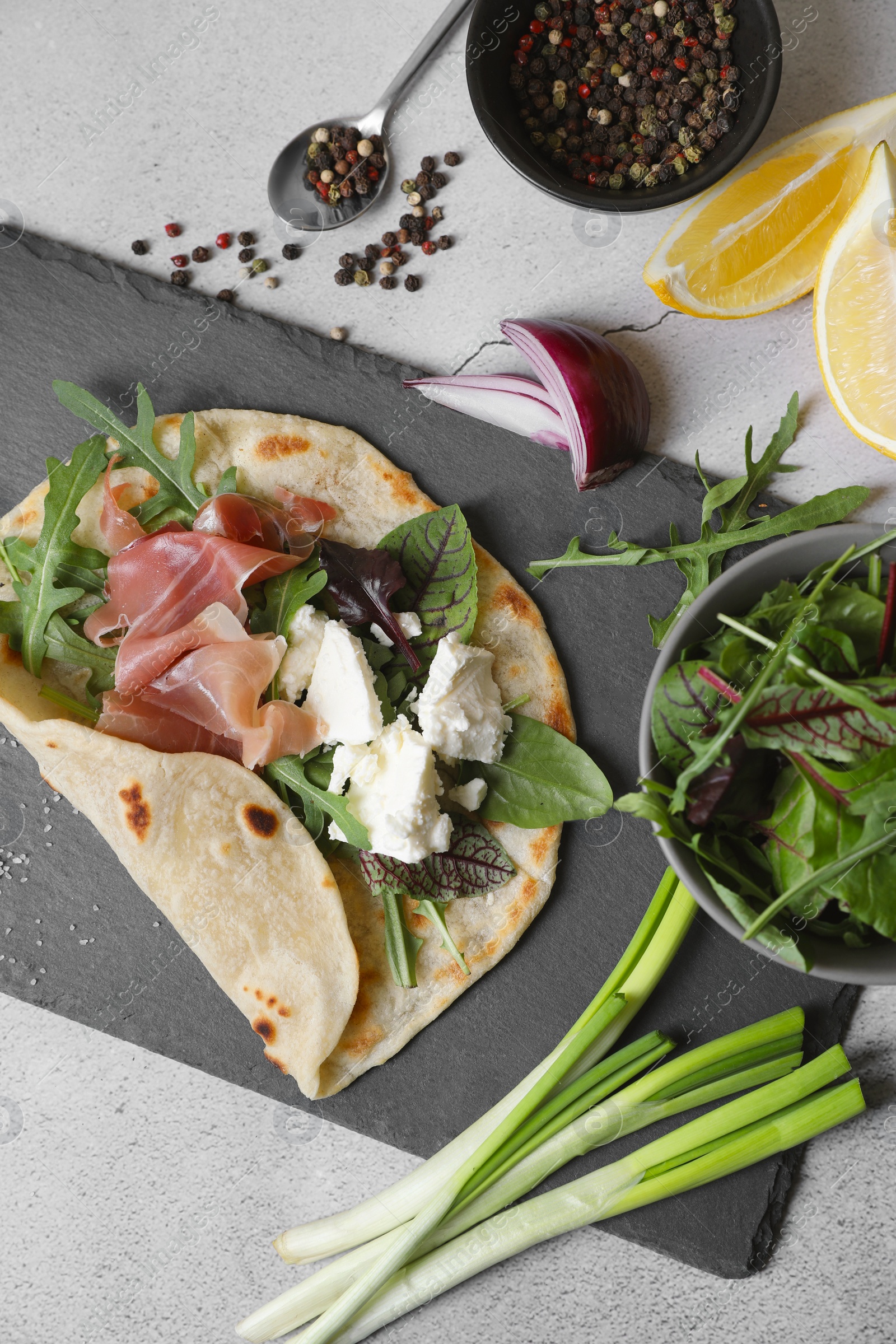 Photo of Delicious pita wrap with jamon, cheese cream and greens on light gray table, flat lay