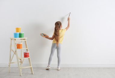 Photo of Little child painting on blank white wall indoors
