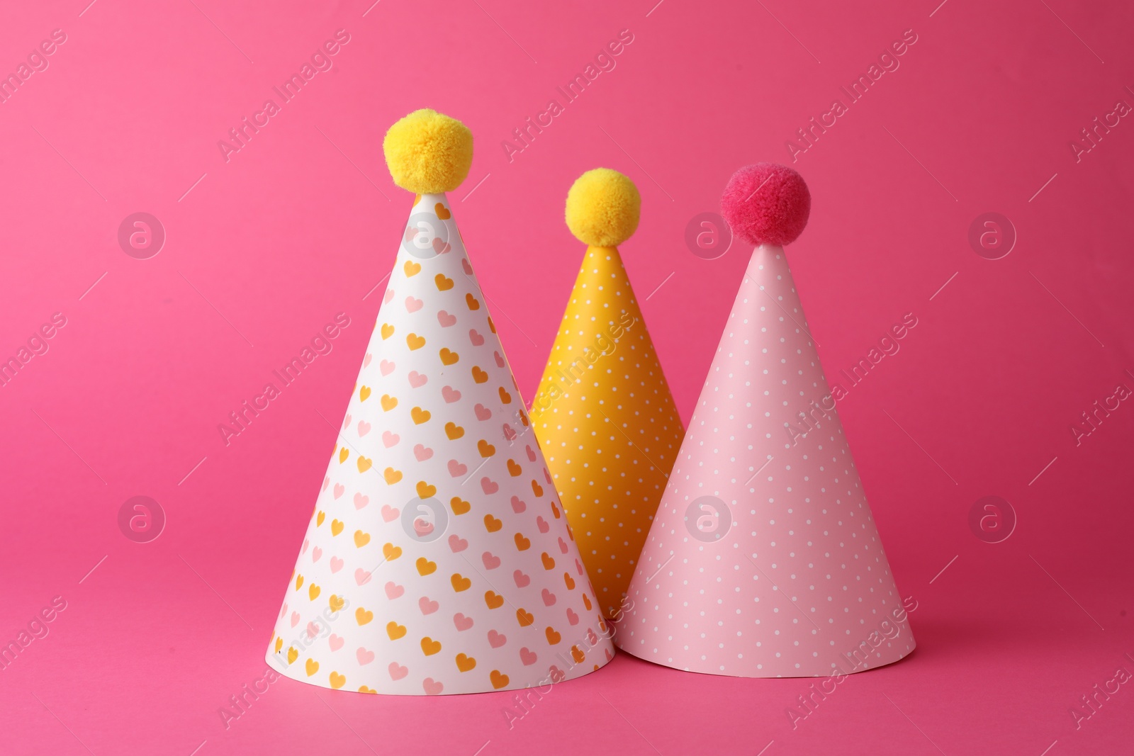 Photo of Beautiful party hats with pompoms on pink background