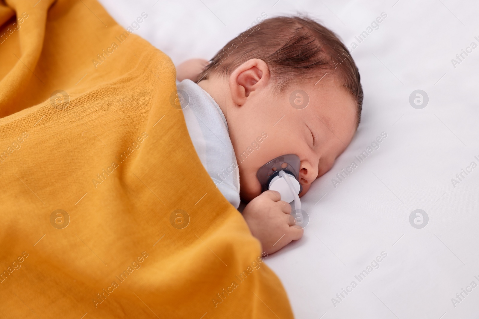 Photo of Cute newborn baby with pacifier sleeping under blanket on bed