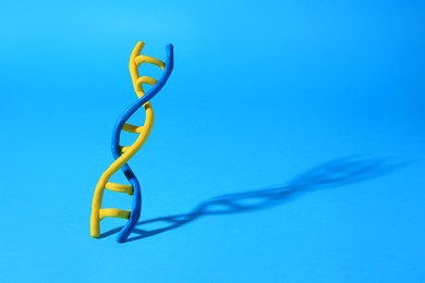 Photo of DNA molecule model made of colorful plasticine on light blue background, space for text