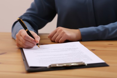 Photo of Businesswoman signing contract at wooden table, closeup of hands