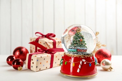 Photo of Beautiful snow globe, gift boxes and Christmas balls on white wooden table