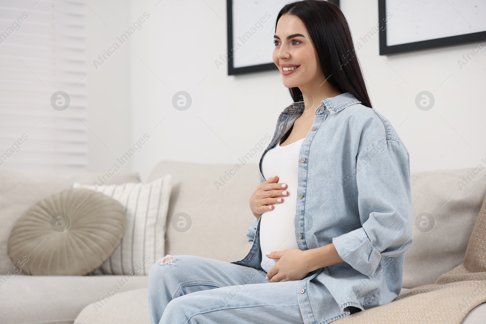 Photo of Happy pregnant woman on sofa at home, space for text