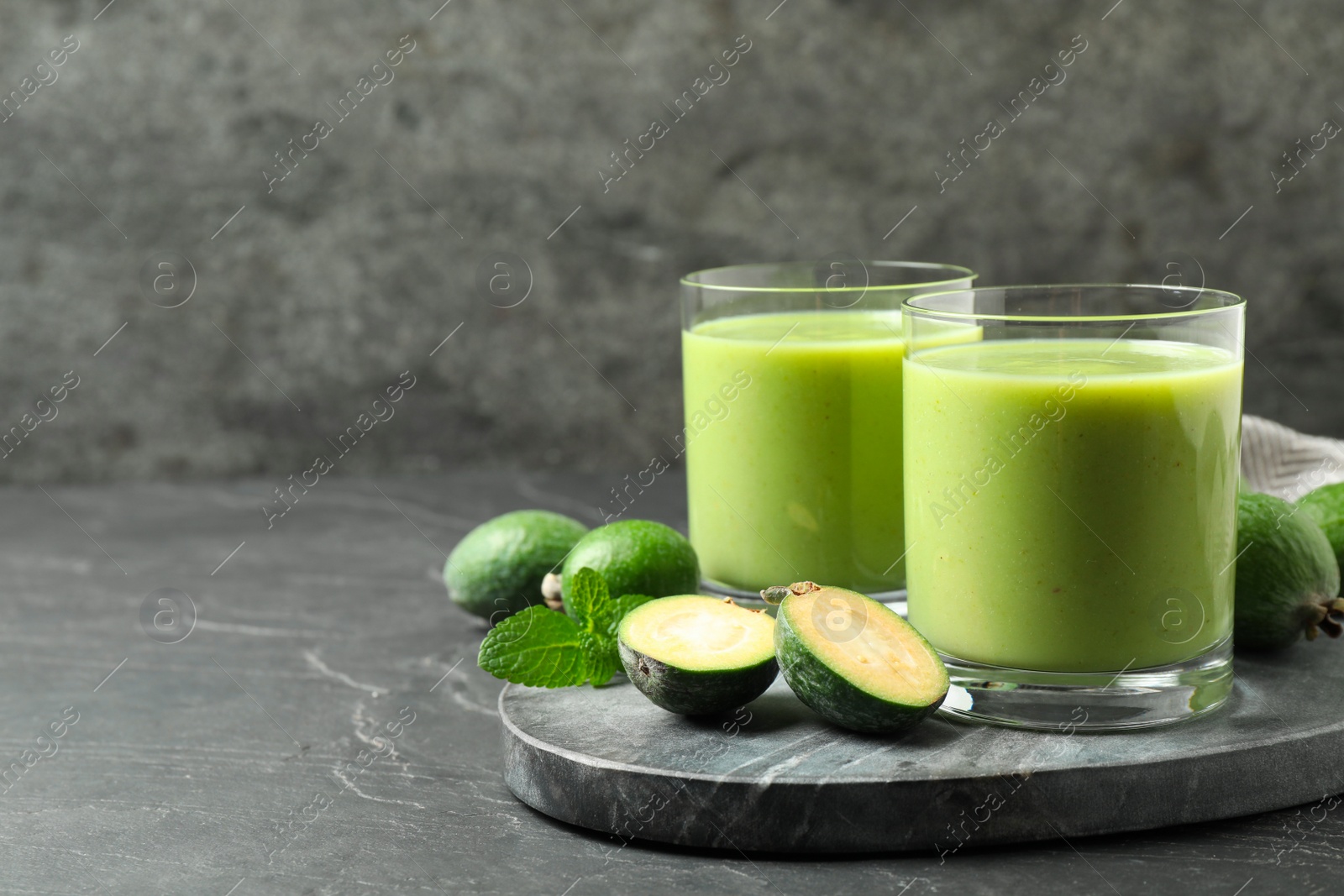 Photo of Fresh feijoa smoothie and fresh fruits on grey table, space for text