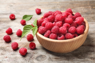 Photo of Bowl with ripe aromatic raspberries on wooden table