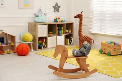 Photo of Stylish child's room interior with cute wooden rocking horse and toys