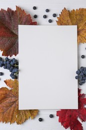 Photo of Flat lay composition with blank card, autumn leaves and grapes on white wooden table. Space for text