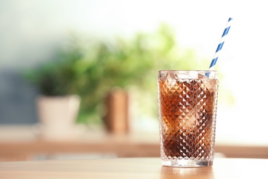 Glass of tasty refreshing cola with ice cubes and straw on table. Space for text