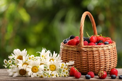 Photo of Wicker basket with different fresh ripe berries and beautiful chamomile flowers on wooden table outdoors