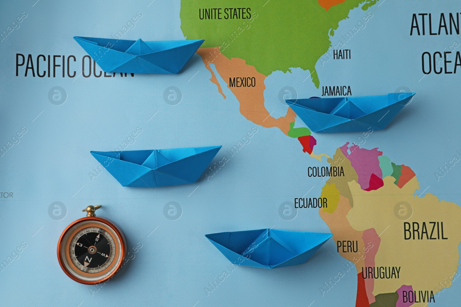 Photo of Bright paper boats and compass on world map, flat lay