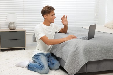 Photo of Happy young man having video chat via laptop on bed indoors