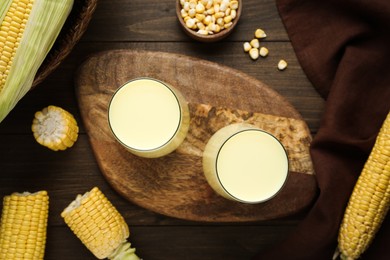 Photo of Tasty fresh corn milk in glasses and cobs on wooden table, flat lay