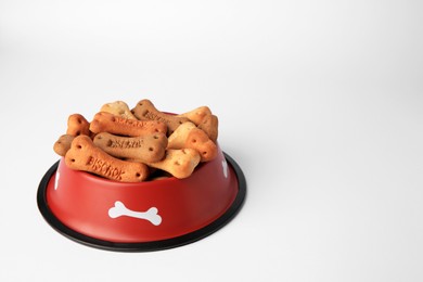 Bone shaped dog cookies in feeding bowl on white background, space for text