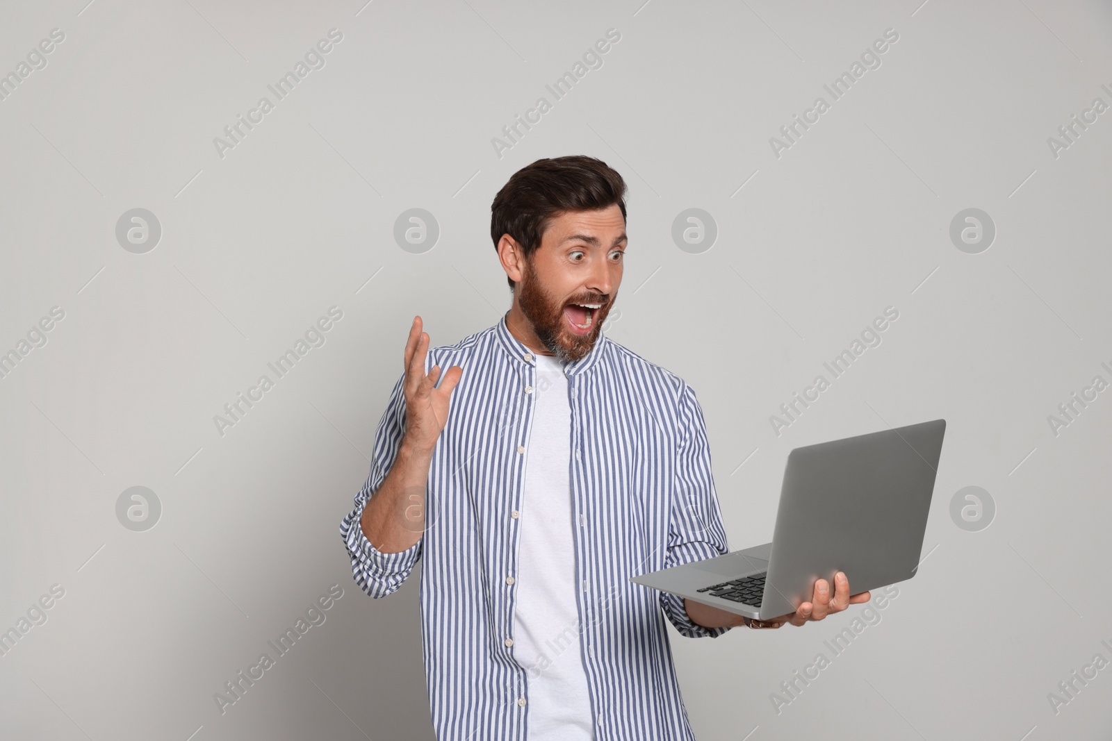 Photo of Emotional bearded man with laptop on light background