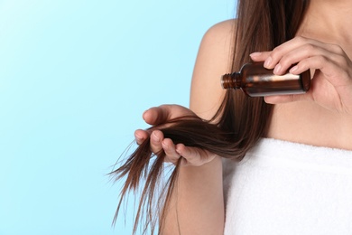 Woman applying oil onto hair against color background, closeup. Space for text