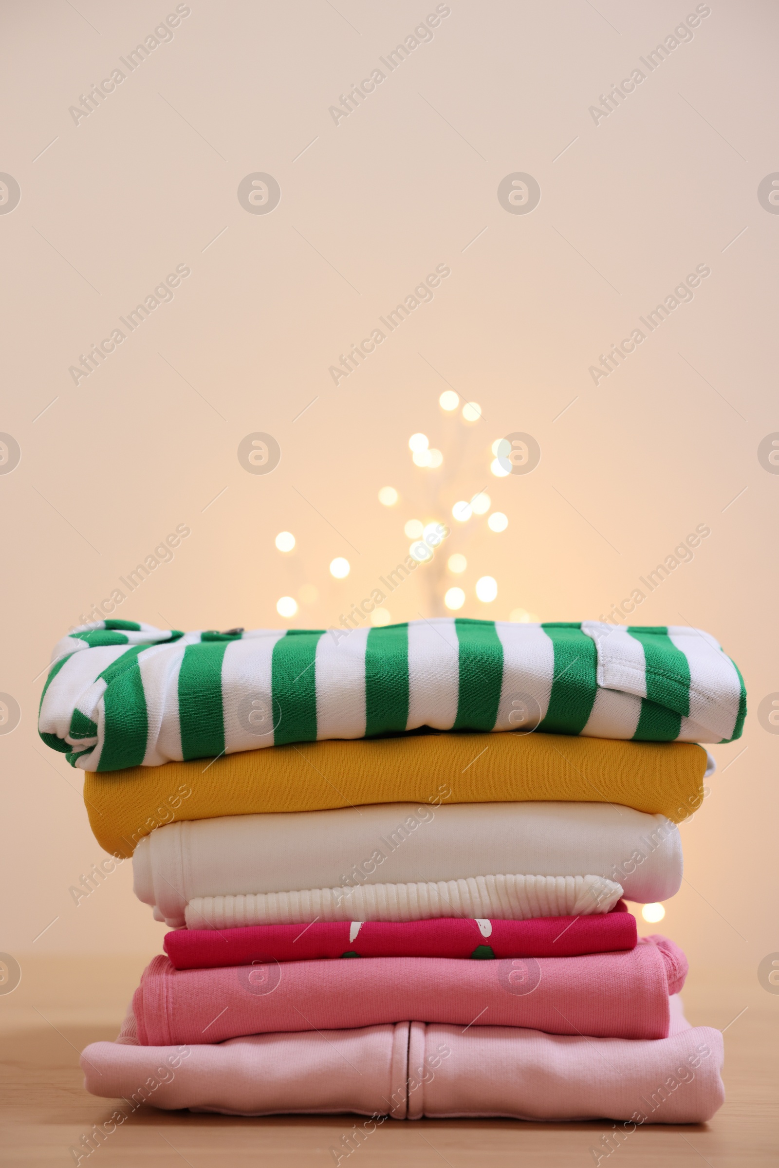 Stack of folded clothes on wooden table against beige background, space for text Photo of Stack of folded clothes on wooden table against beige background, space for text