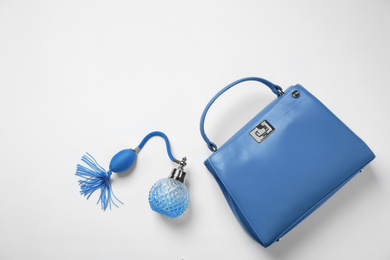 Photo of Stylish purse and perfume bottle on white background, top view. Classic blue - color of the Year 2020