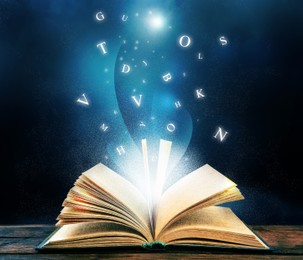 Open book with magic light and glowing letters flying out of it on wooden table against black background